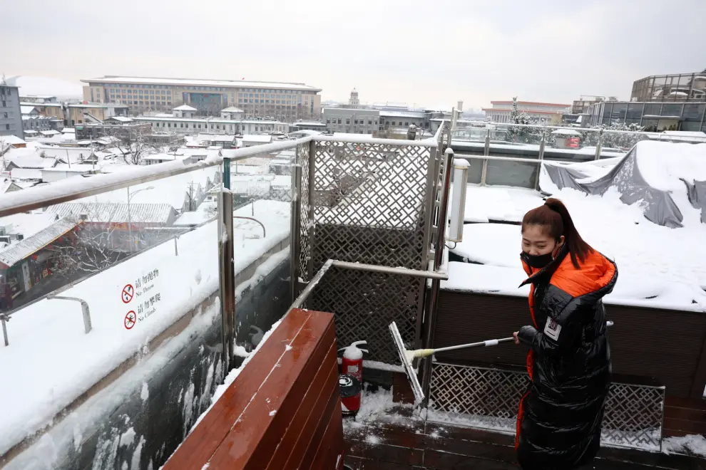 A staff member sweeps snow from a bench at a rooftop of a restaurant, on a snowy day in Beijing, China December 11, 2023. REUTERS/Tingshu Wang [[[REUTERS VOCENTO]]]