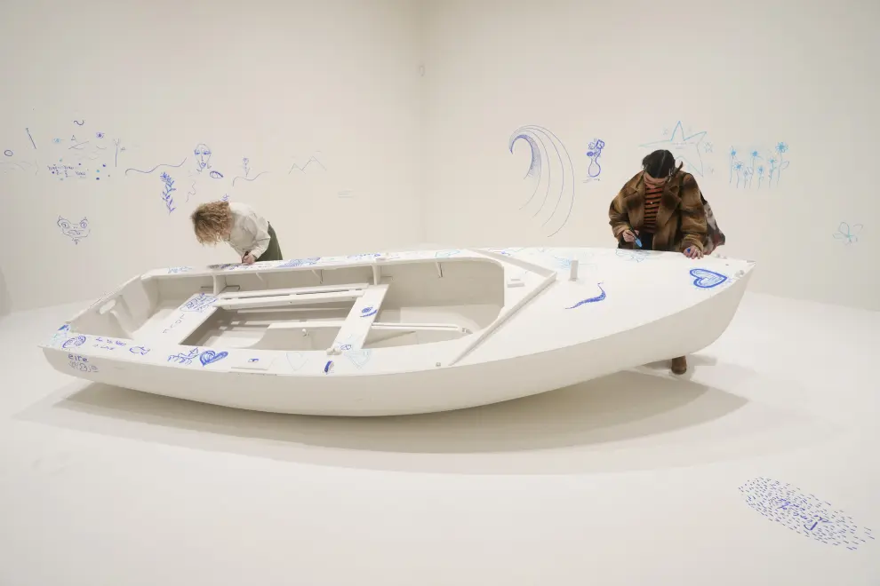 Members of staff draw on a work entitled Add Colour (Refugee Boat), Concept 1960, first realised 2016, exhibition realisation 2024, at the Yoko Ono : Music of the Mind exhibition at the Tate Modern, the works of art are copyright Yoko Ono, In London, Tuesday, Feb. 13, 2024. The exhibition which has many pieces that are interactive and the public and which participate in, runs from Feb.15, to Sept. 1. (AP Photo/Alastair Grant)