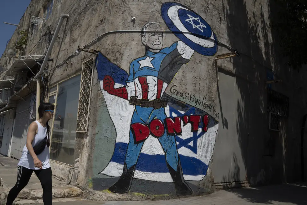 Una mujer pasa delante de un mural en una calle de Tel Aviv que representa al presidente estadounidense Joe Biden como un superhéroe que defiende a Israel