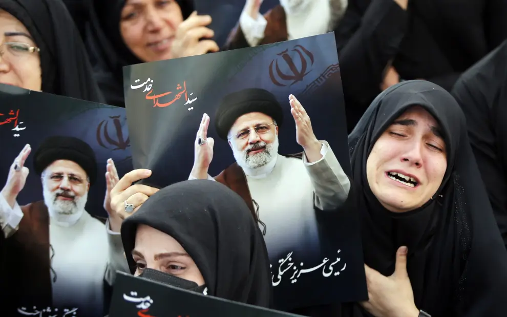 Mujeres iraníes vestidas con chadores negros sostienen carteles del fallecido presidente Ebrahim Raisi mientras participan en una ceremonia de luto en Teherán