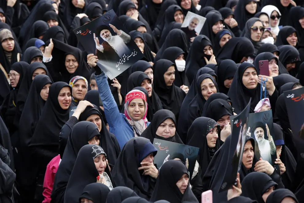 Mujeres iraníes vestidas con chadores negros sostienen carteles del fallecido presidente Ebrahim Raisi mientras participan en una ceremonia de luto en Teherán