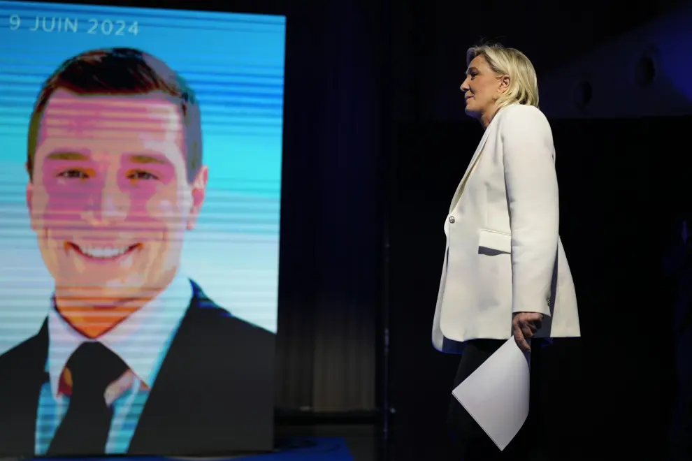 French far-right leader Marine Le Pen walks past a screen showing the president of the French far-right National Rally Jordan Bardella at the party election night headquarters after French President Emanuel Macron announced he dissolves National Assembly and calls new legislative election after defeat in EU vote, Sunday, June 9, 2024 in Paris. First projected results from France put far-right National Rally party well ahead in EU elections, according to French opinion poll institutes. (AP Photo/Lewis Joly)