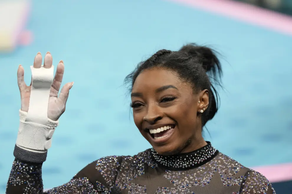 Simone Biles, of United States, waves from the competition floor before competing on the uneven bars during a women's artistic gymnastics qualification round at Bercy Arena at the 2024 Summer Olympics, Sunday, July 28, 2024, in Paris, France. (AP Photo/Abbie Parr)