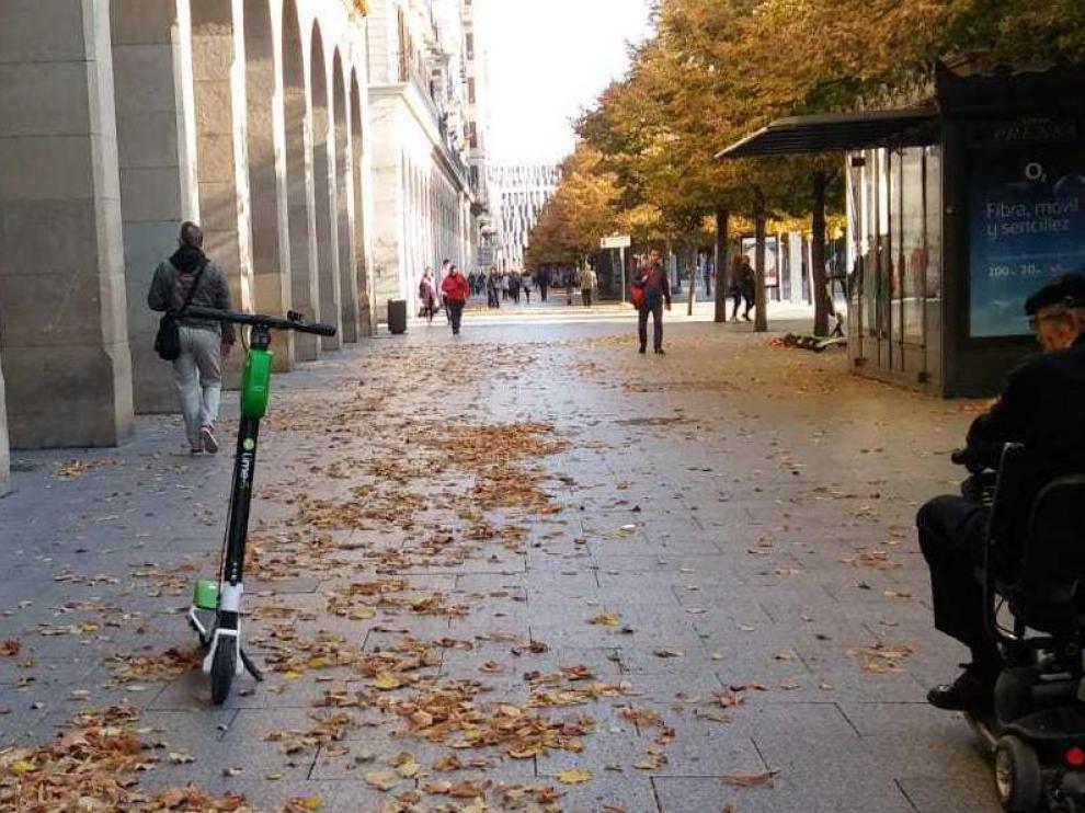 Un hombre en silla de ruedas mira un patinete eléctrico de alquiler abandonado en plena acera, en el paseo de Independencia de Zaragoza este lunes.