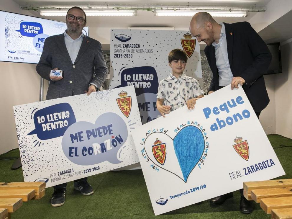Eduardo Olivares, el niño de 7 años ganador del premio de dibujo de la Federación de Peñas del Real Zaragoza, posa junto al vicepresidente Sainz de Varanda y el responsable de Marquetin, Carlos Arranz con las réplicas de los abonos y pequeabonos de la temporada 2019-20.