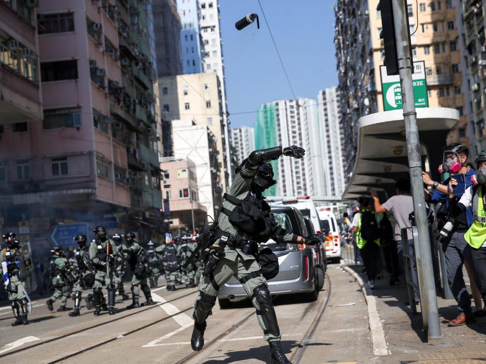 Un policía lanza una granada de gas contra manifestantes en una calle de Hong Kong.