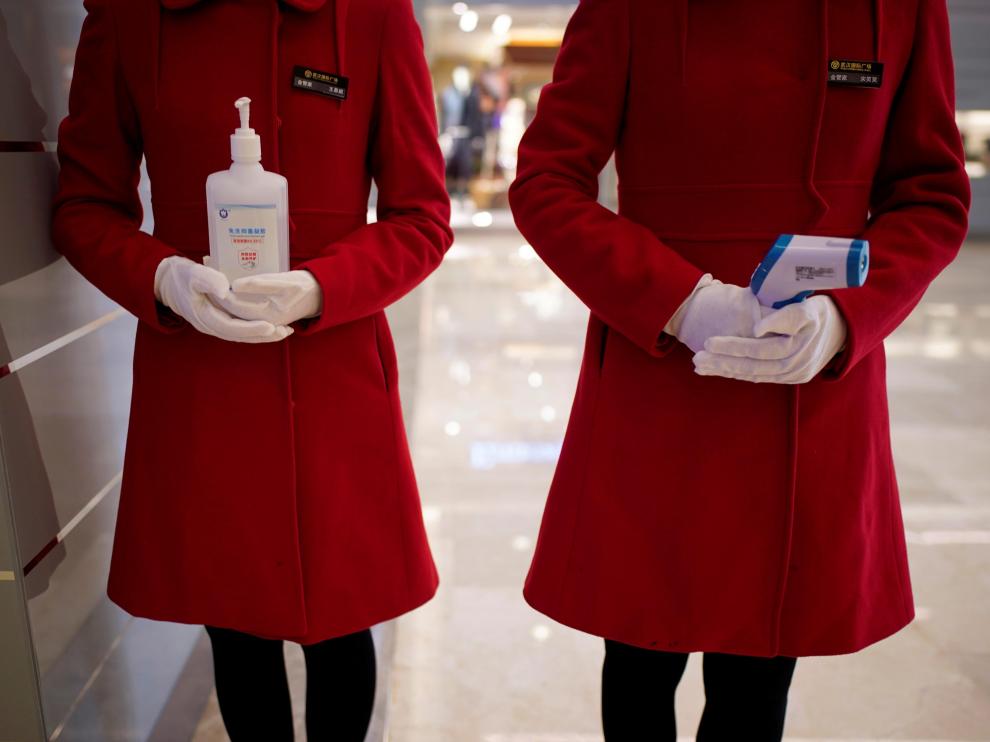 Dos empleadas de un centro comercial de Wuhan esperan a clientes con gel desinfectante y un termómetro.