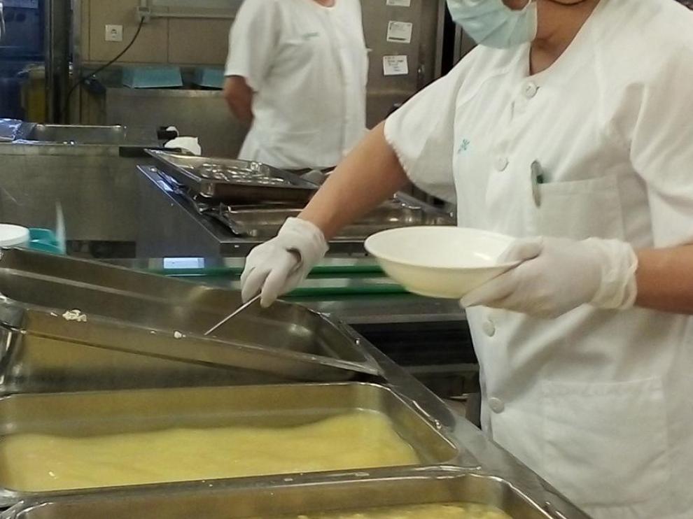 Una de las trabajadoras de la cocina del Servet sirve una ración en un plato.