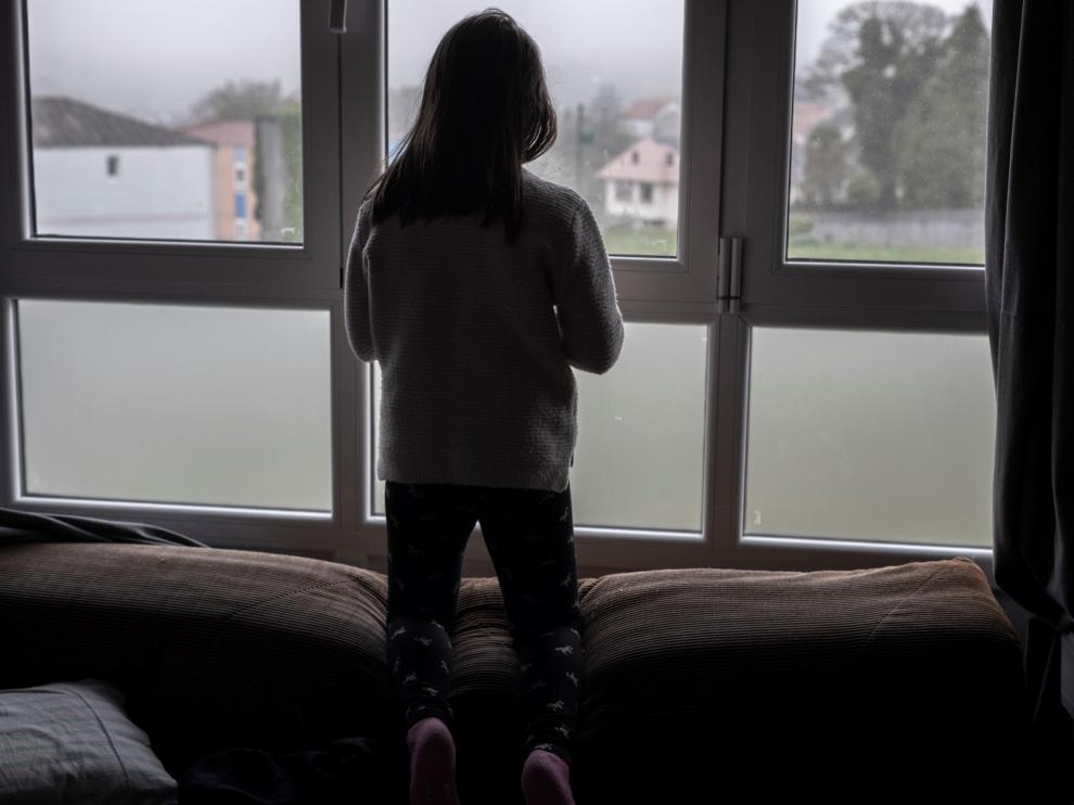 Una niña asomada a la ventana de su casa.