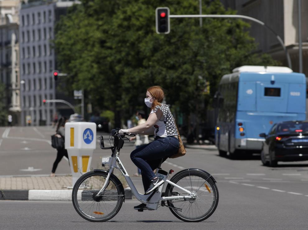 Una mujer protegida con mascarilla monta en una bicicleta.