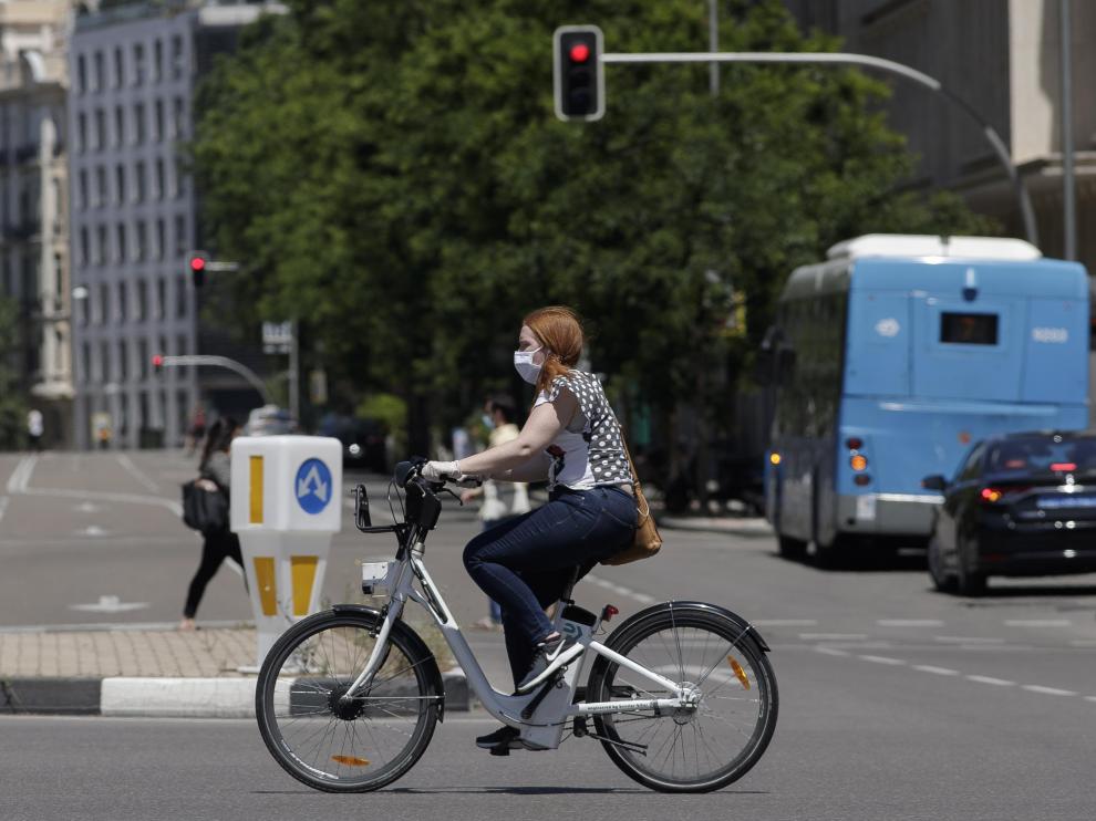 Una mujer protegida con mascarilla monta en una bicicleta.