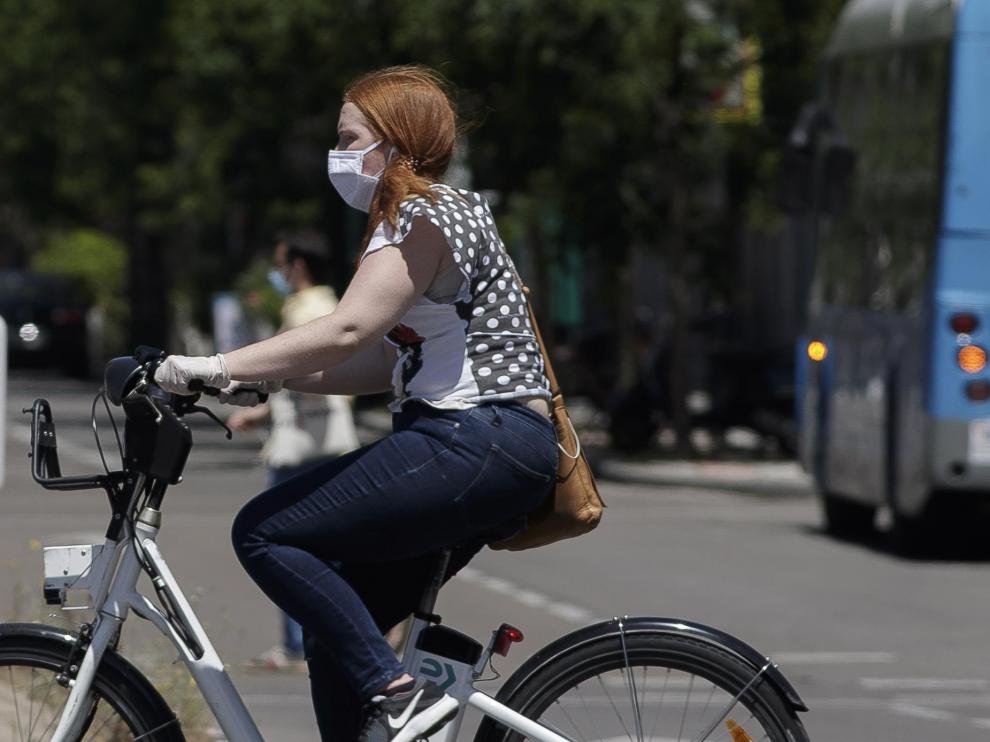 Una mujer protegida con mascarilla monta en una bicicleta.