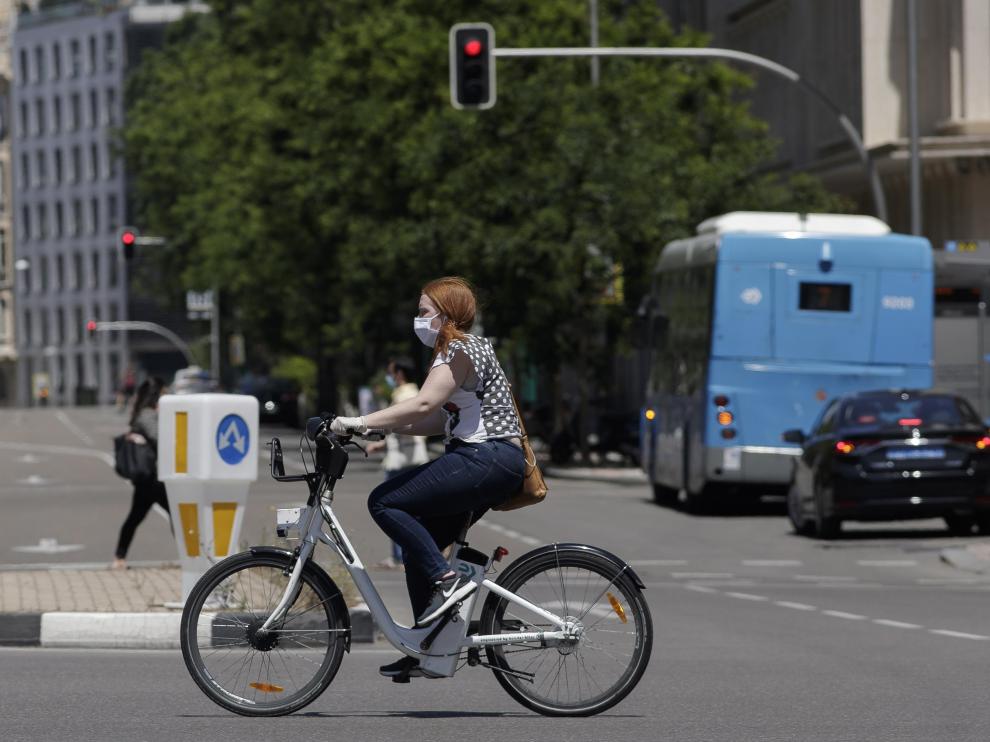 Una mujer protegida con mascarilla monta en una bicicleta.