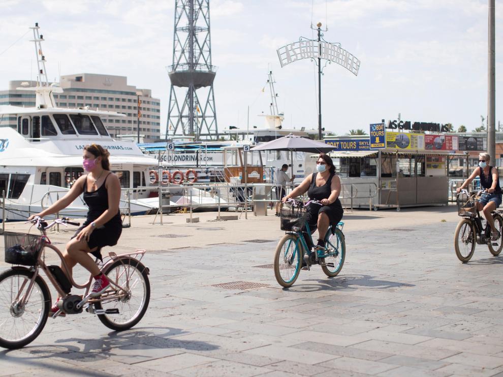 Tres turistas pasean por el puerto de Barcelona con bicicleta.