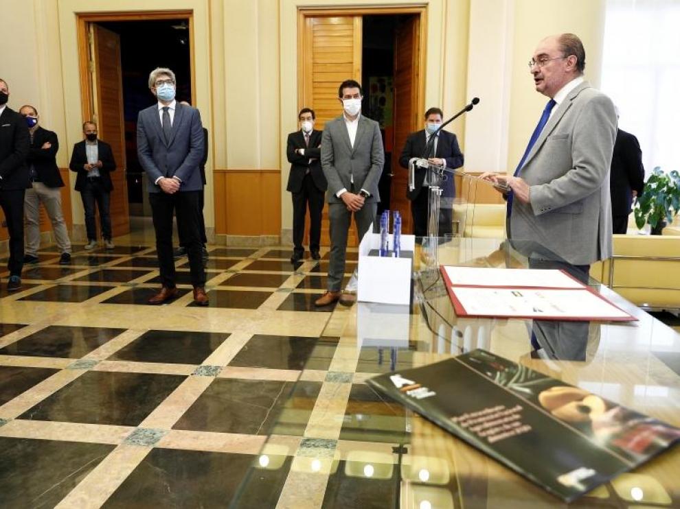 Javier Lambán firma en acuerdo, con los representantes de las siete cadenas de distribución al fondo.