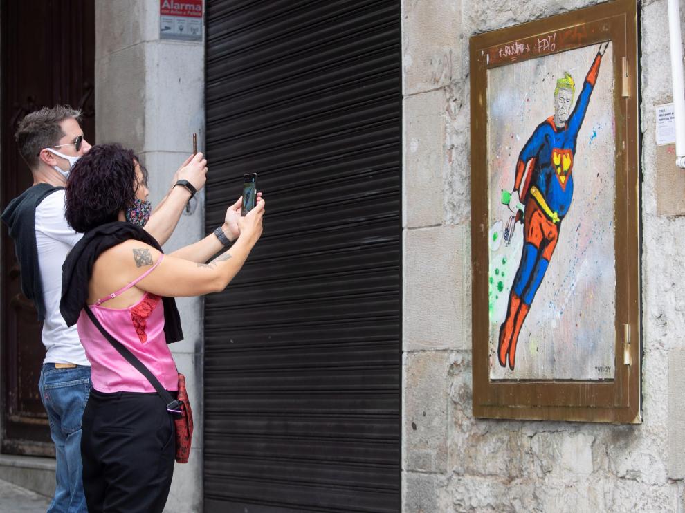 Dos personas fotografían un grafitti en una pared de Barcelona que representa a Trump vestido de Superman.
