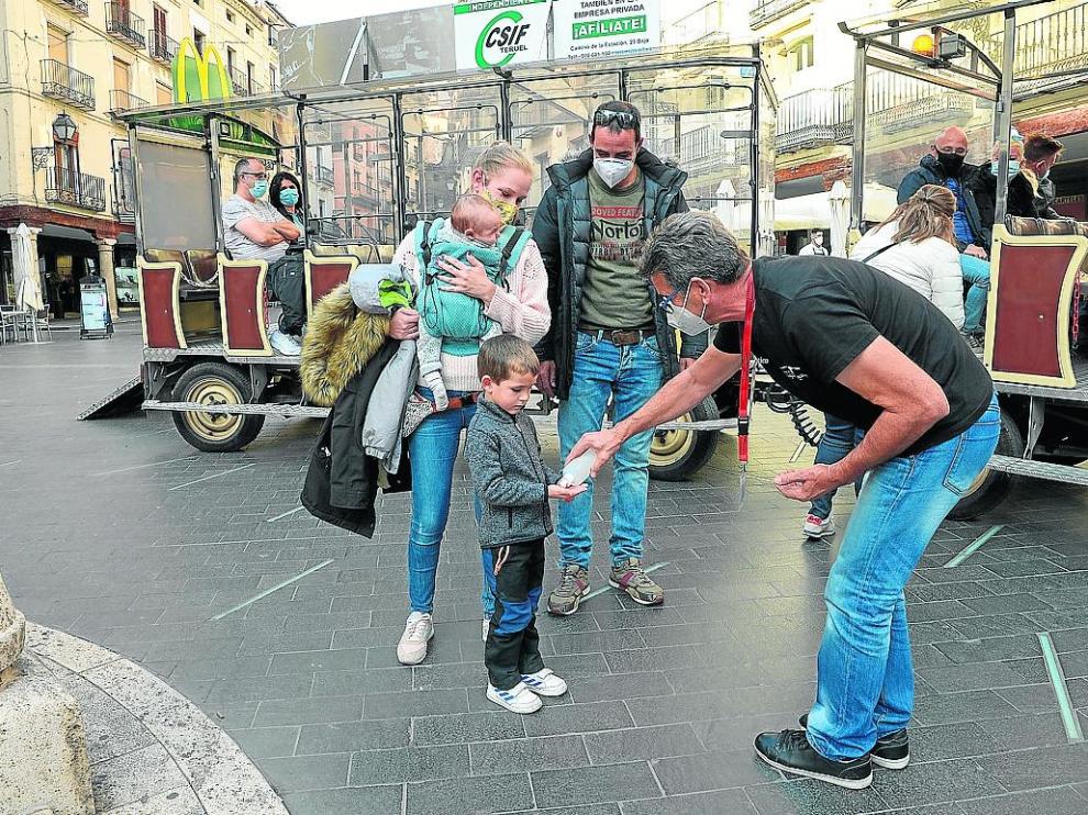 Los turistas limpian sus manos antes de subir al tren turístico en la plaza del Torico de Teruel.