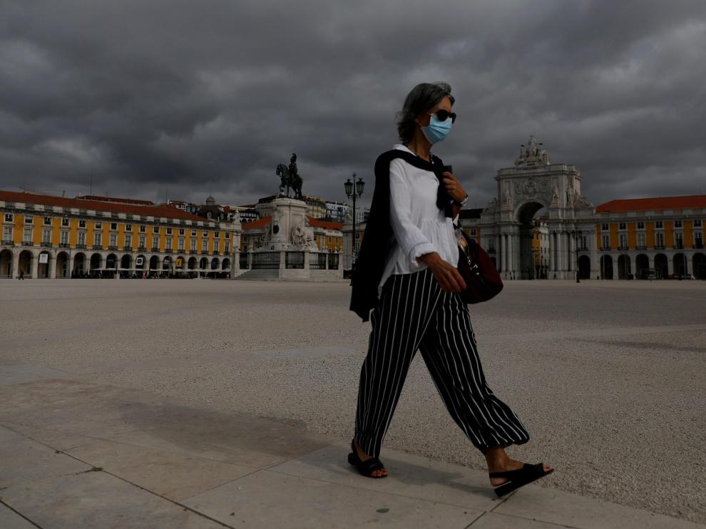 Una mujer protegida con una máscara camina por una vacía plaza del Comercio, en Lisboa.