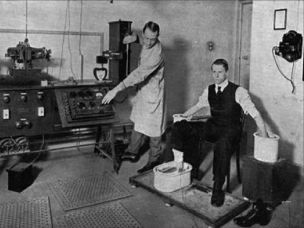 Willem Einthoven prueba el galvanómetro de hilo con un paciente, con manos y pies desnudos dentro de cubetas de disolución salina (1916)