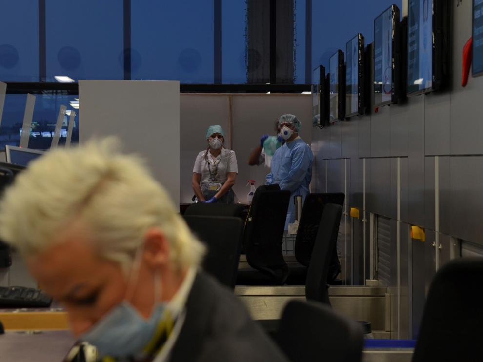 Una empleada del aeropuerto de Viena factura maletas mientras dos especialistas esperan para realizar test rápidos de antígenos.