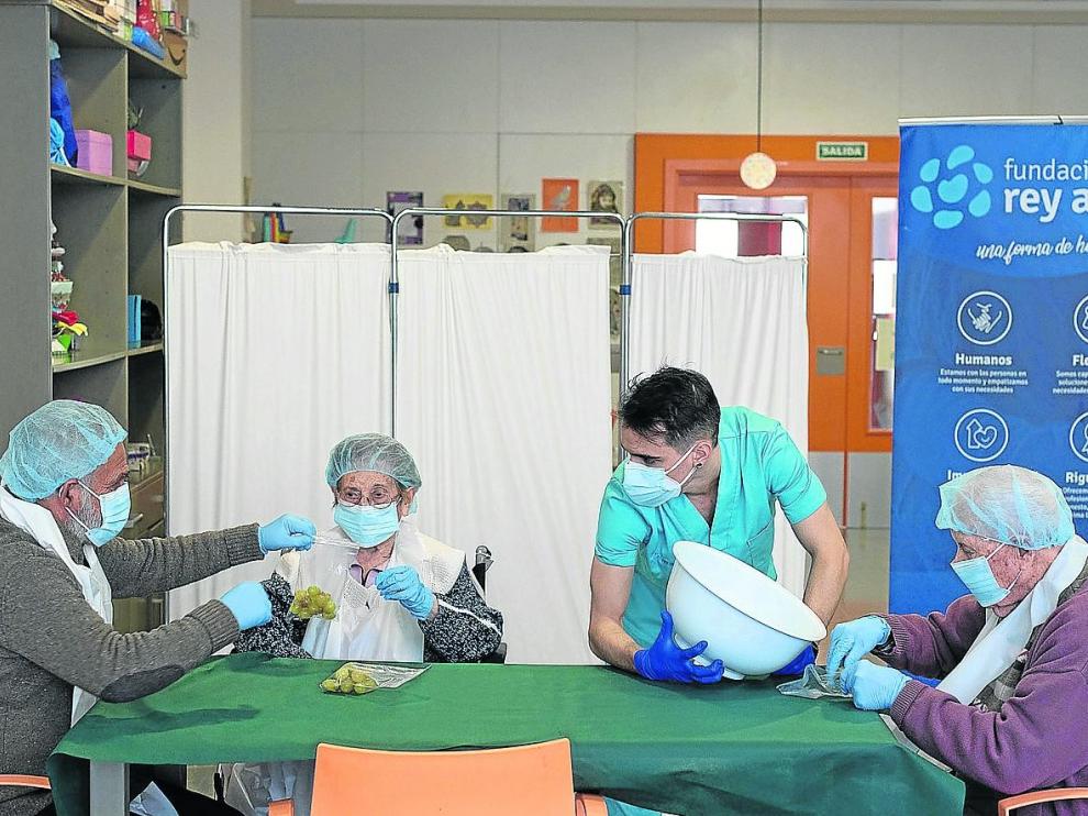 S. C. Juan Durán, Gloria Grima y Eduardo Royo, con el terapeuta ocupacional Lucas García, preparan las uvas para esta Nochevieja