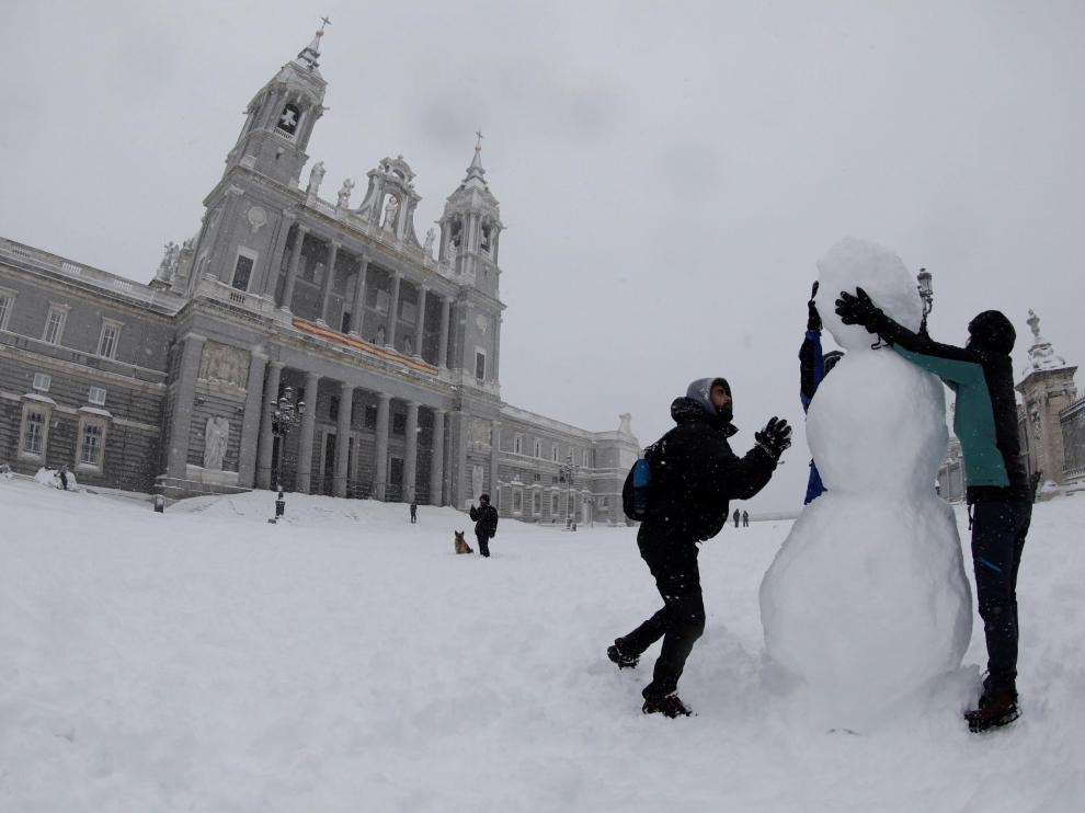 Dos personas hacen un muñeco de nieve en las inmediaciones de la Catedral de la Almudena, en Madrid.
