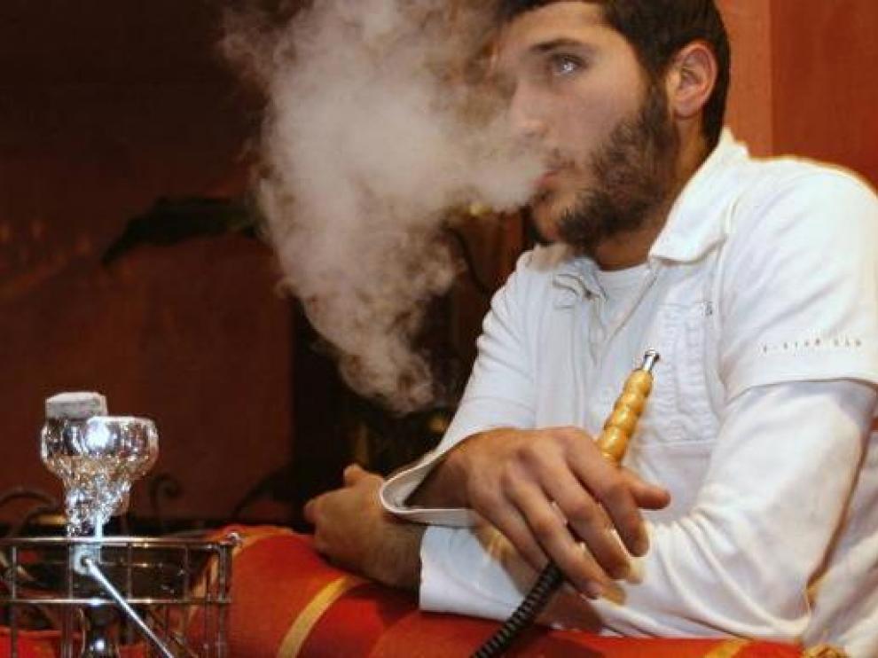 Un joven fuma tabaco con una cachimba en un café de París.