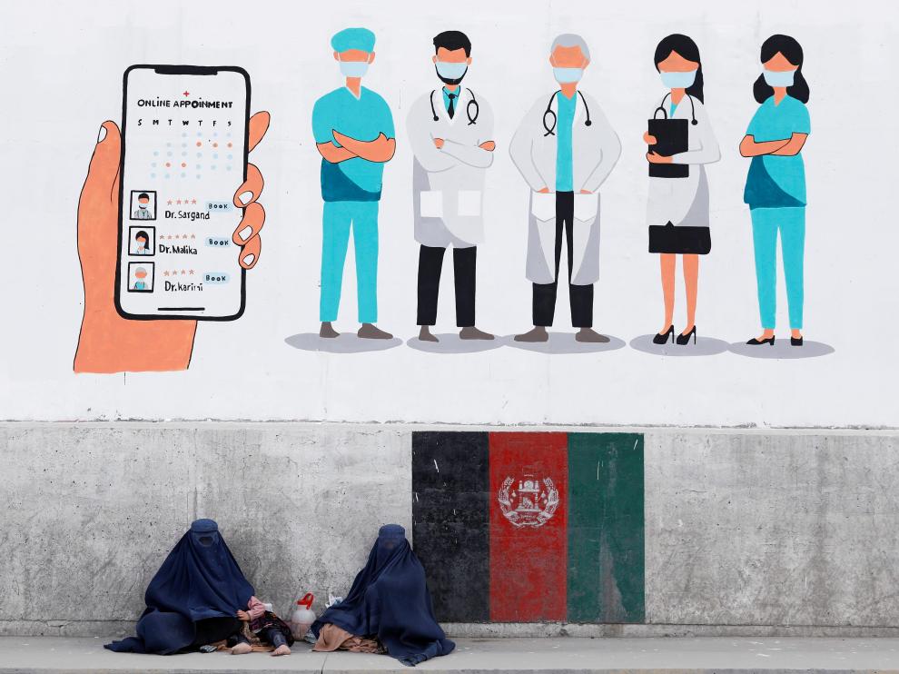 FILE PHOTO: Afghan women clad in burqa Beg under graffiti on a wall, in Kabul