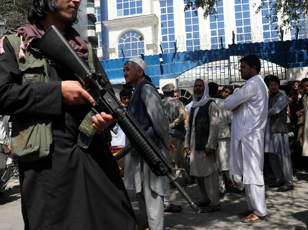 Un miembro de seguridad talibán vigila la fila de personas frente al Banco Azizi de Kabul, en Afganistán