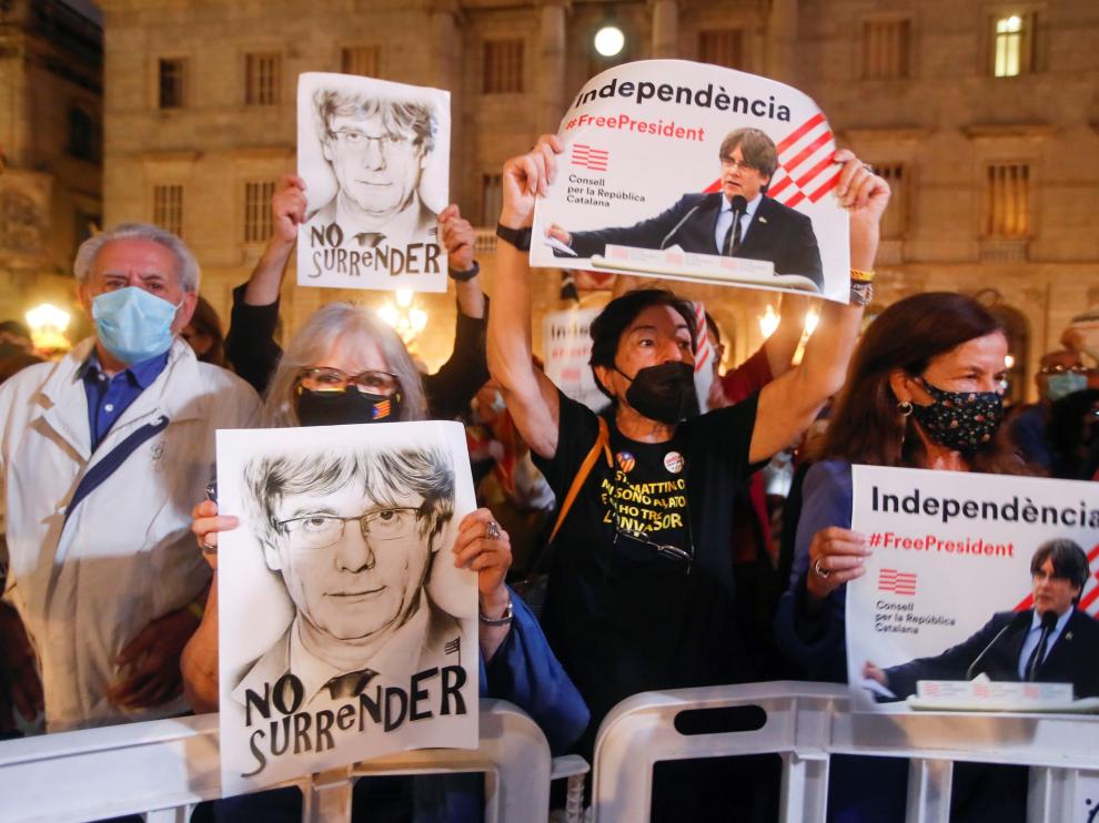 Varias personas sostienen retratos del expresidente de la Generalitat Carles Puigdemont en Barcelona.