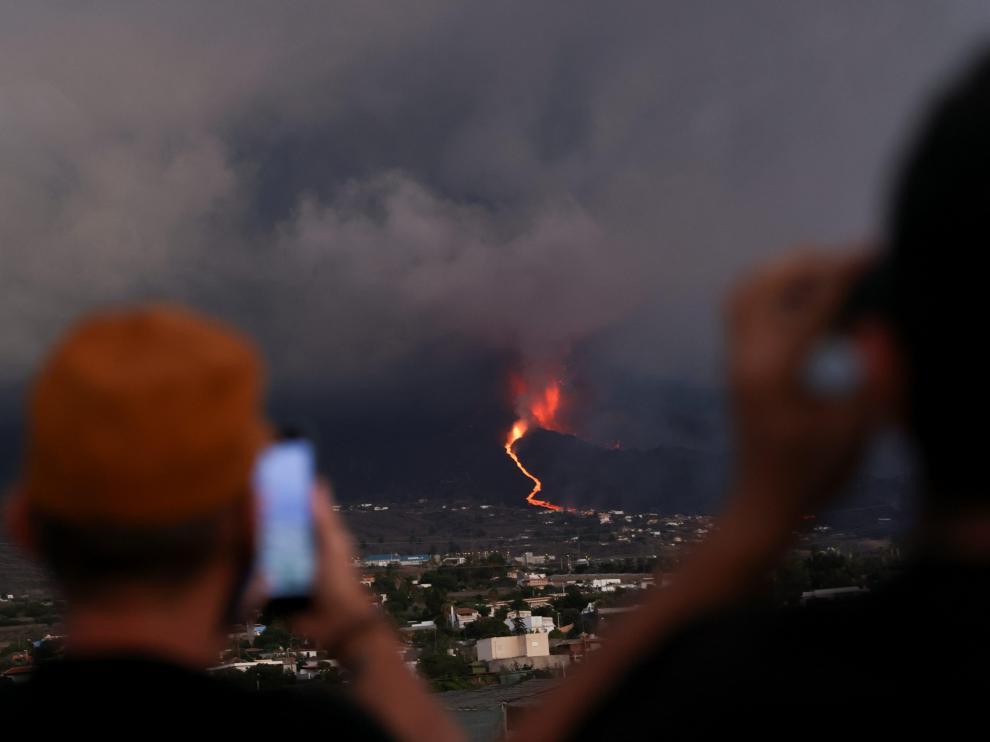 Dos personas miran cómo desciende la lava por la ladera del volcán
