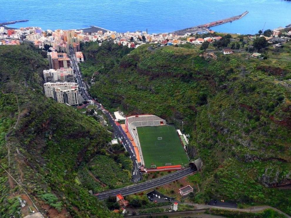 Vista aérea del estadio Silvestre Carrillo de Santa Cruz de La Palma. Es el final de una cuesta de 1 km, junto a la montaña, en un barranco. Al fondo, la capital palmera, con el océano y el puerto.