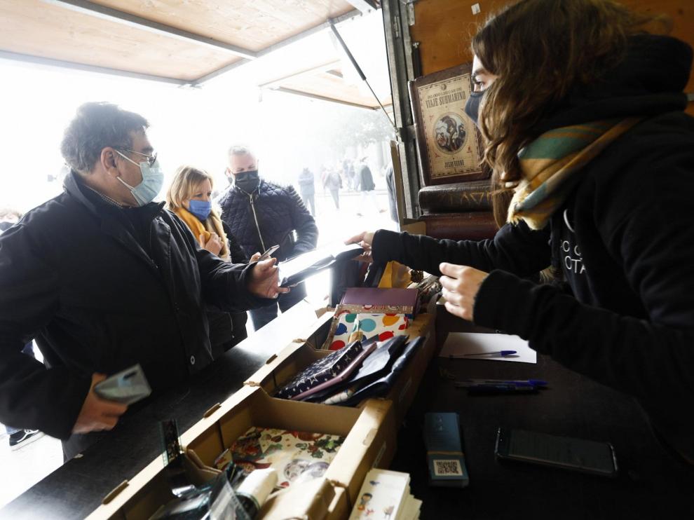 Lucía Pitarch, de Atrapavientos, entrega su libro a un lector que acudió este domingo a la plaza del Pilar