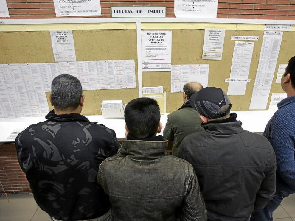 Unos desempleados se interesan por las posibles ofertas de trabajo en una oficina del Inem.