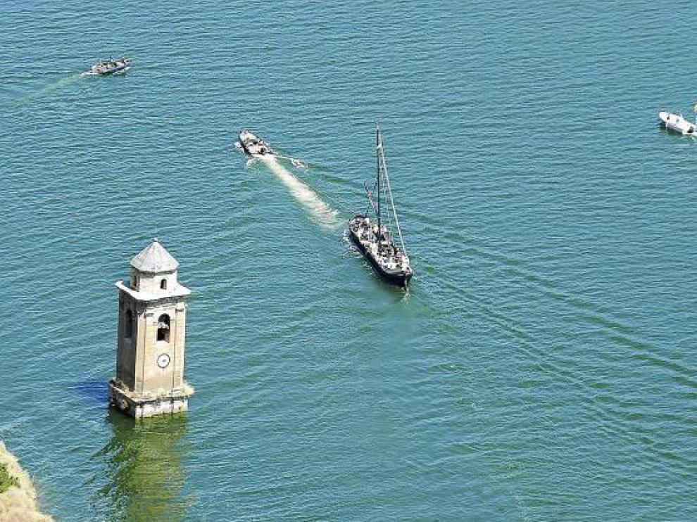 El llaüt 'Cardenal' pasa junto a la torre de la iglesia que quedó bajo las aguas del embalse.