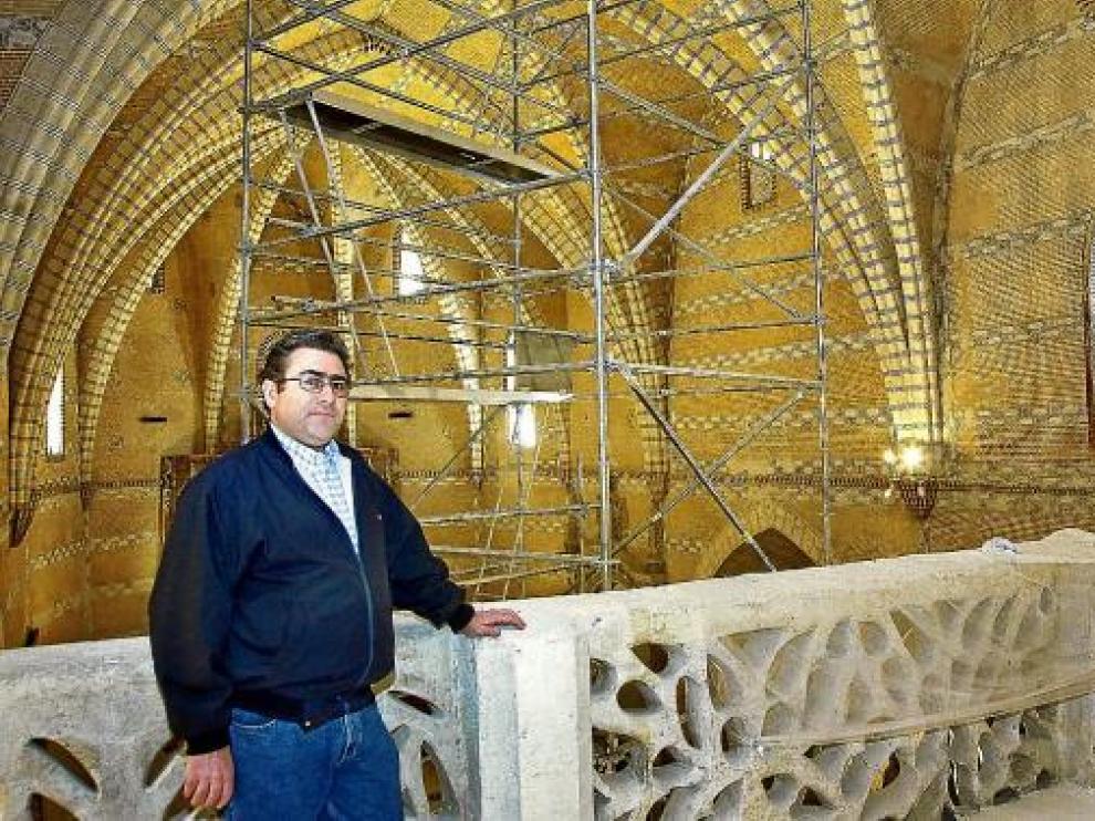 El párroco de la iglesia posa delante del andamio que sujeta el arco con problemas estructurales.