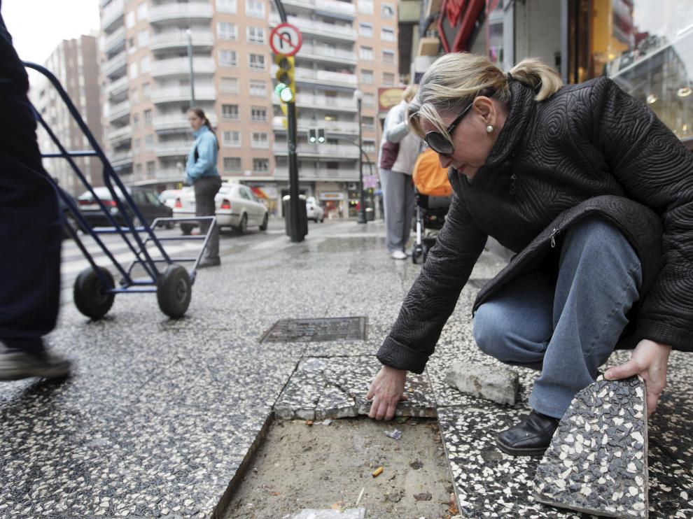 Mª Ángeles Dehesa muestra el hueco de una de las baldosas rotas, junto a otras inestables.