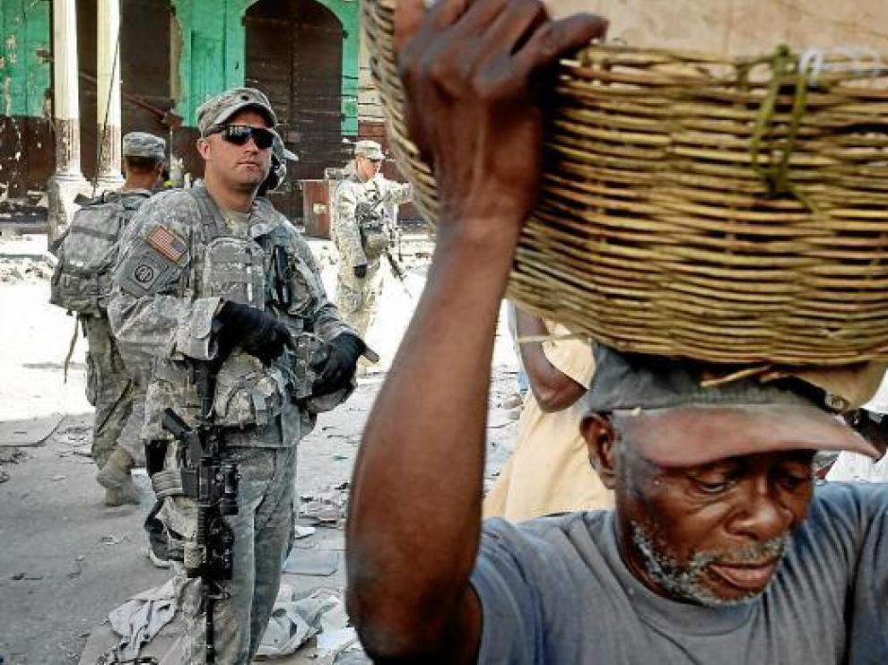 Un haitiano carga con un cesto en Puerto Príncipe ante la mirada de un soldado estadounidense.