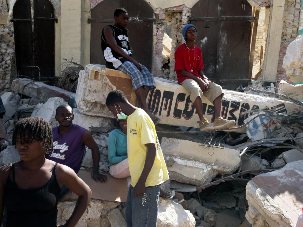 Varios ciudadanos haitianos junto a los escombros de un edificio derruído por el terremoto