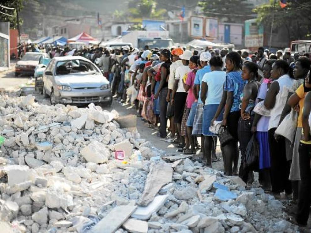 Los haitianos hacen fila para recibir alimentos junto a unos escombros, ayer en Puerto Príncipe