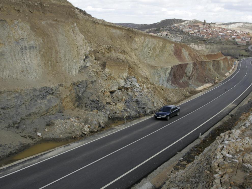 Un coche pasa junto al talud que sufre desprendimientos. Al fondo, el casco urbano de Palomar de Arroyos.
