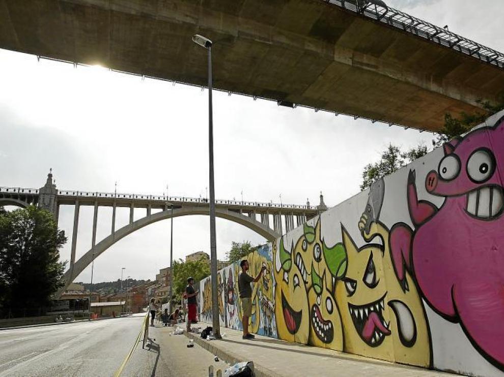 Los grafiteros, durante su trabajo sobre la tapia del Asilo de San Julián. En primer término, la obra ganadora del concurso.