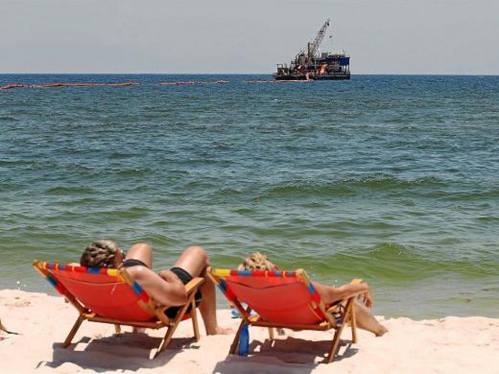 Dos bañistas toman el sol mientras continúan los trabajos de limpieza del crudo, en Alabama.