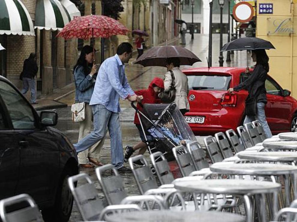Los oscenses se refugian de la lluvia bajo los paraguas, mientras las terrazas se quedan vacías.