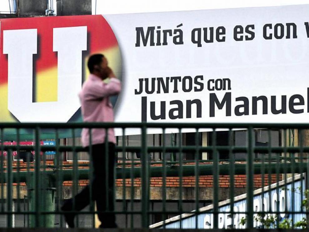 Un hombre habla por el móvil mientras camina frente a una valla publicitaria del candidato Juan Manuel Santos, ayer en Cali.