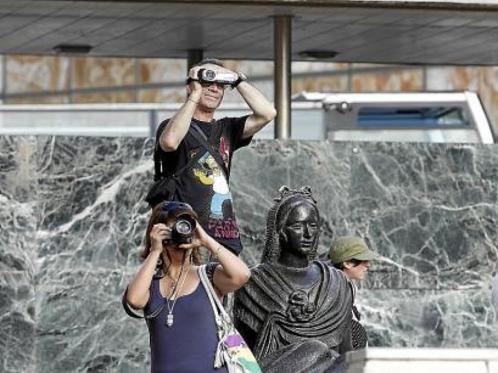 Dos turistas, cámara en mano, inmortalizan la plaza del Pilar de Zaragoza.