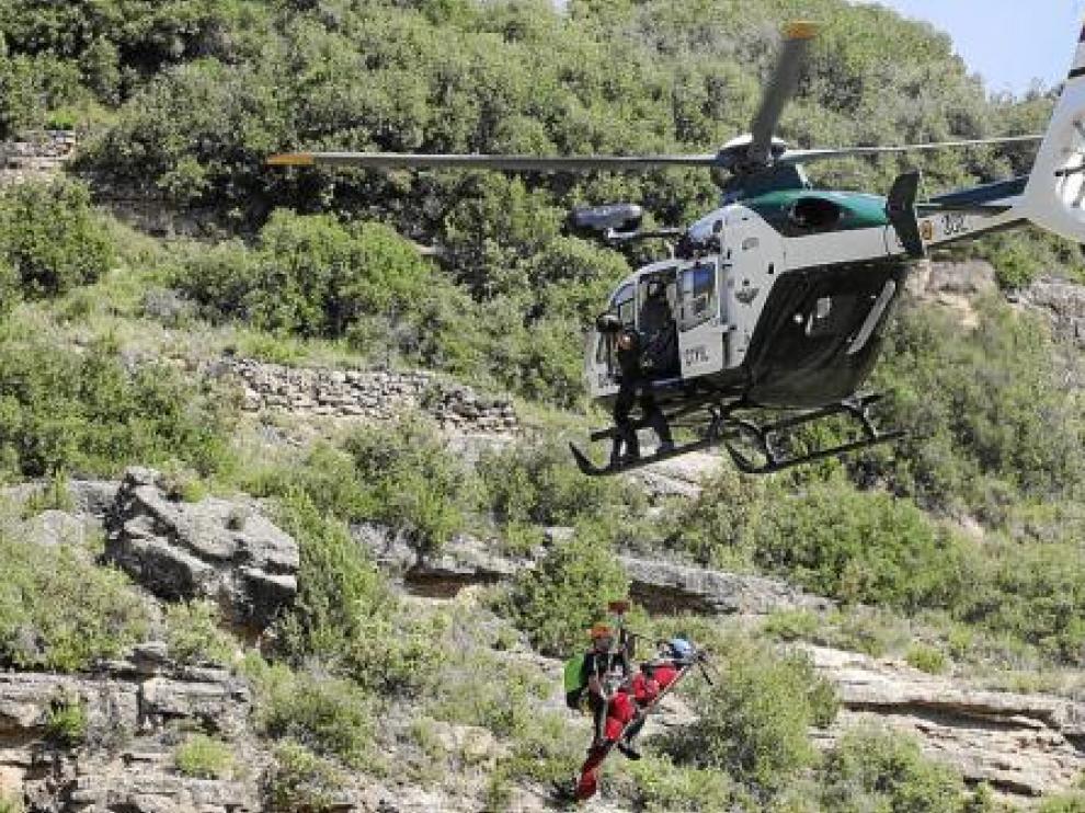 El helicóptero traslada con la grúa a un herido (de rojo) que va acompañado de un agente.