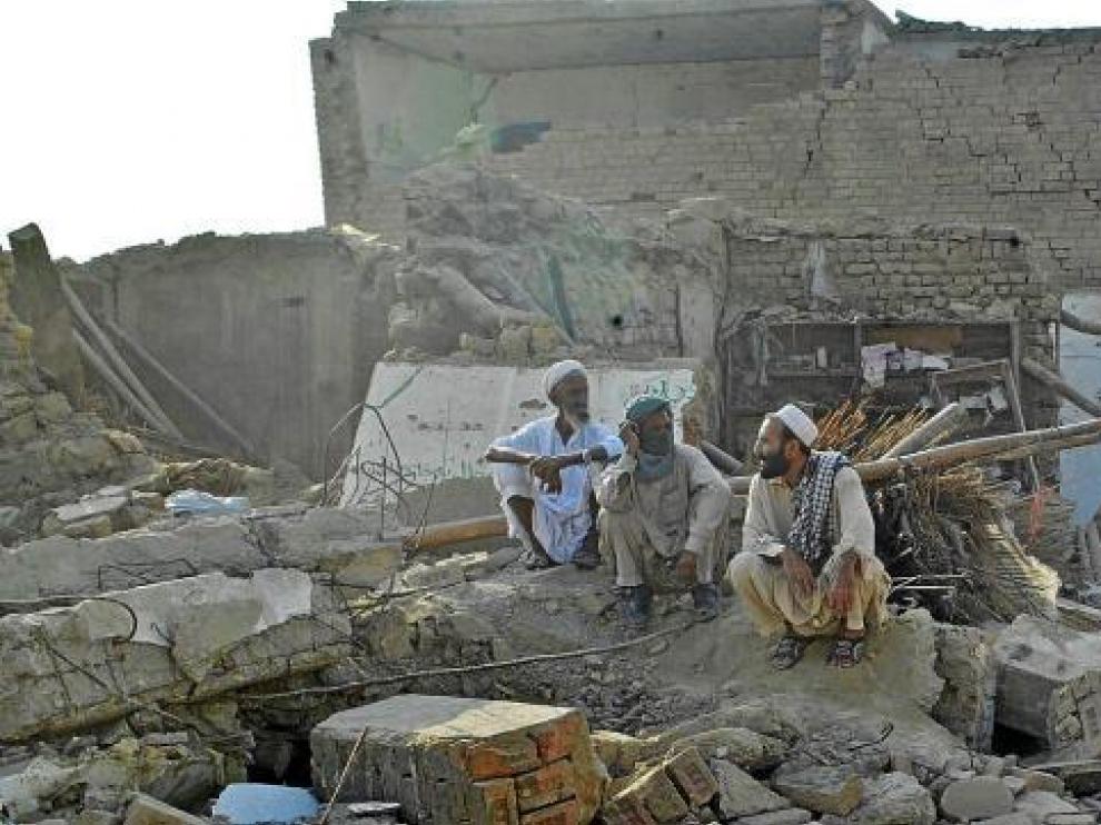 Tres hombres paquistaníes descansan entre las ruinas cercanas al lugar del atentado.
