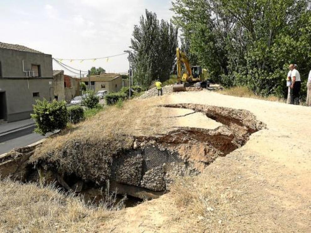 A la izquierda de la sima, varias viviendas. A la derecha, varios técnicos miran hacia el río.