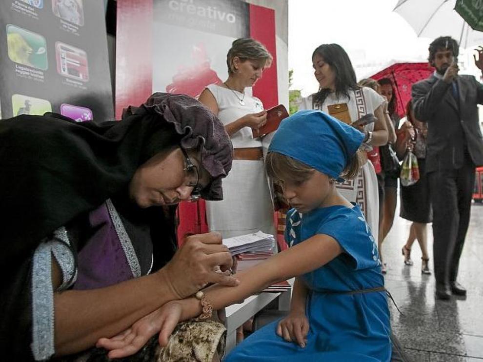 La venezolana Carol Ceva realiza un tatuaje de henna con palabras celtibéricas a María Cebrián, ayer en plena lluvia en Zaragoza.